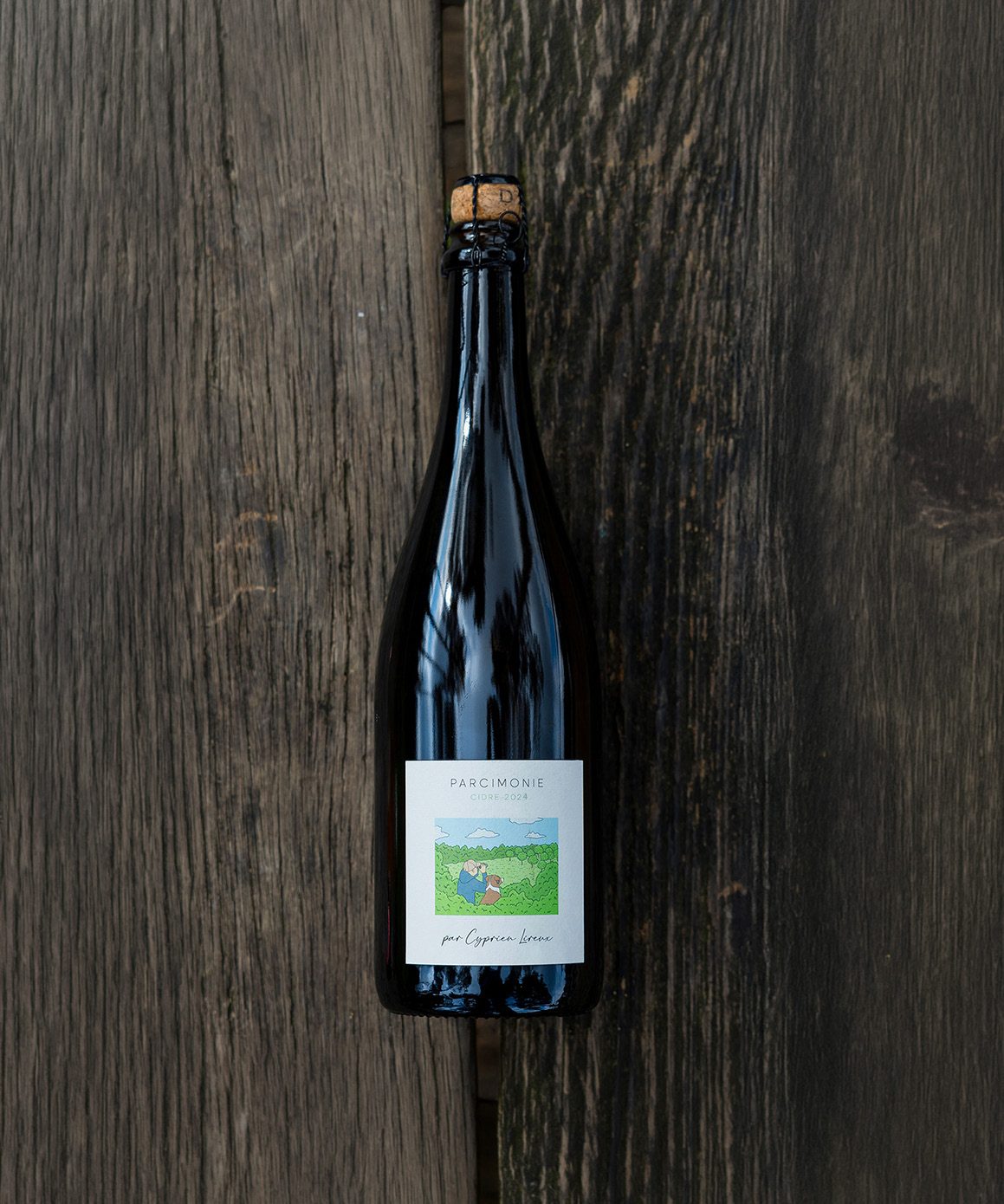 A bottle of Parcimonie 2024 lying on dark weathered wood, cork and cage catching the light