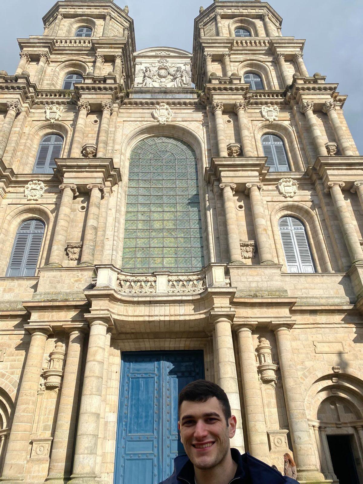 Yiannis at the blue doors of Rennes cathedral, its carved granite facade towering above