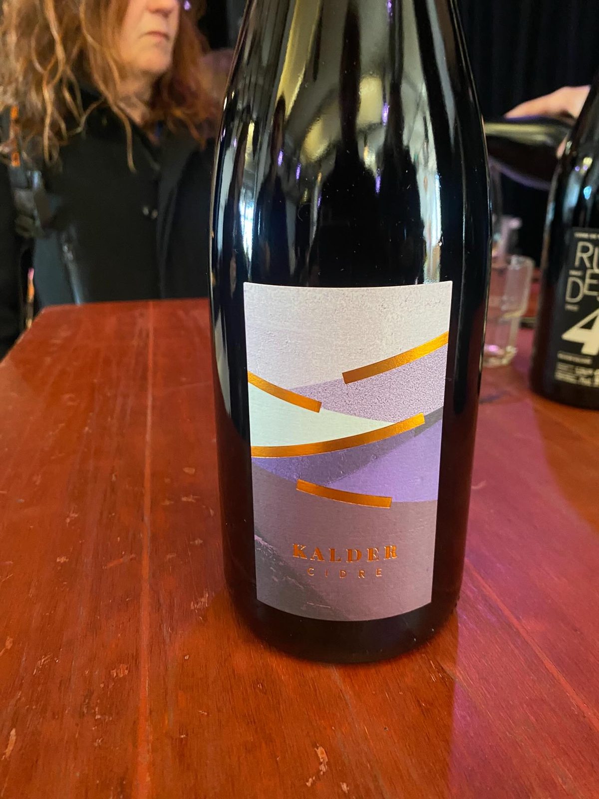 A bottle of Kalder Cidre with a geometric purple and orange landscape label