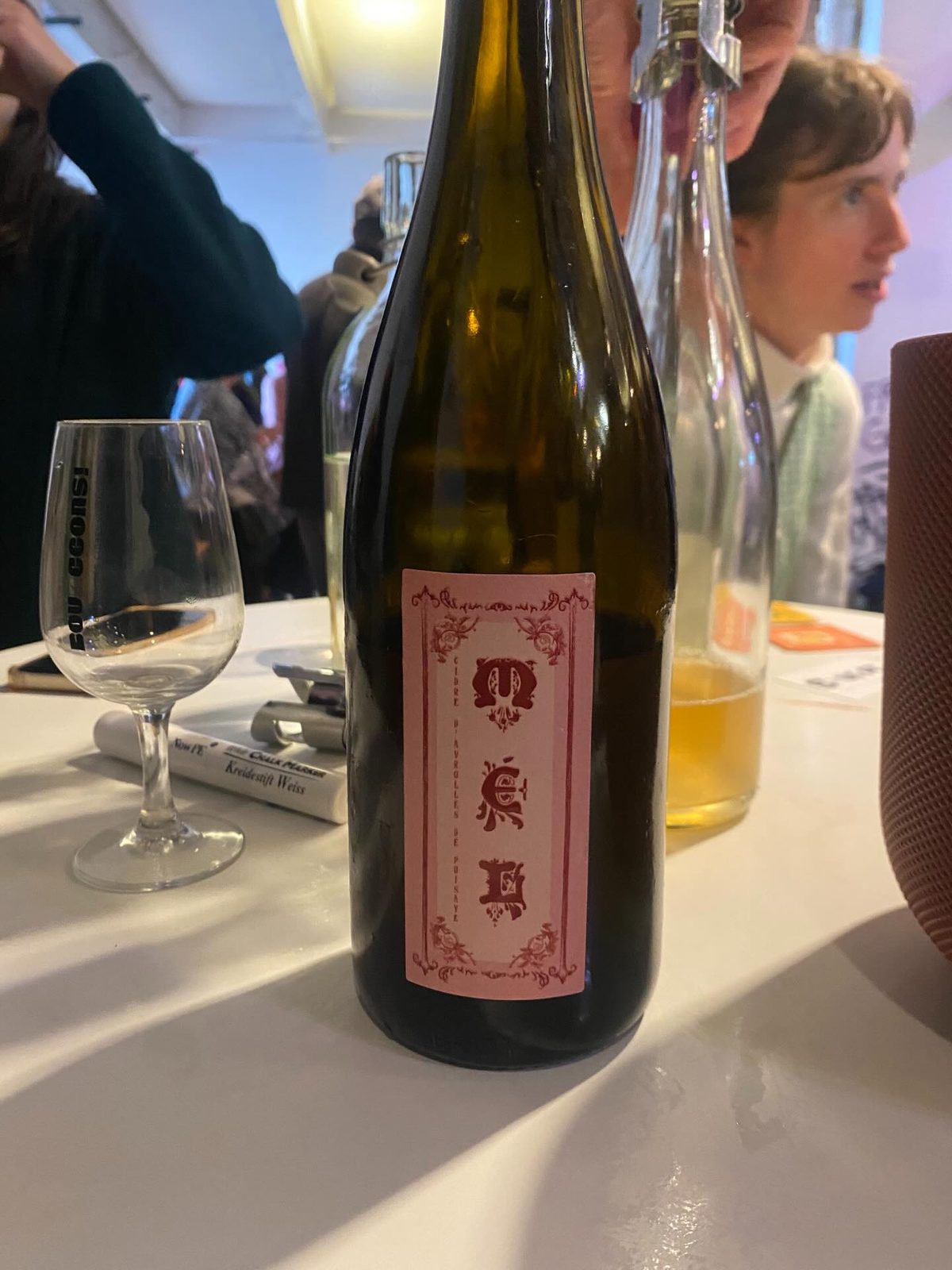 A bottle of MEL Cidre d'Avrolles de Puisaye with a pink illustrated label on a tasting table