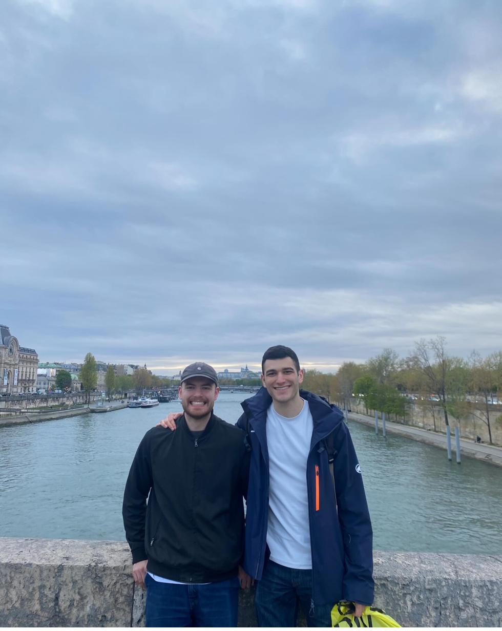 Isaac and Yiannis on a bridge over the Seine in Paris on a grey spring evening, with the Musée d'Orsay on the left bank
