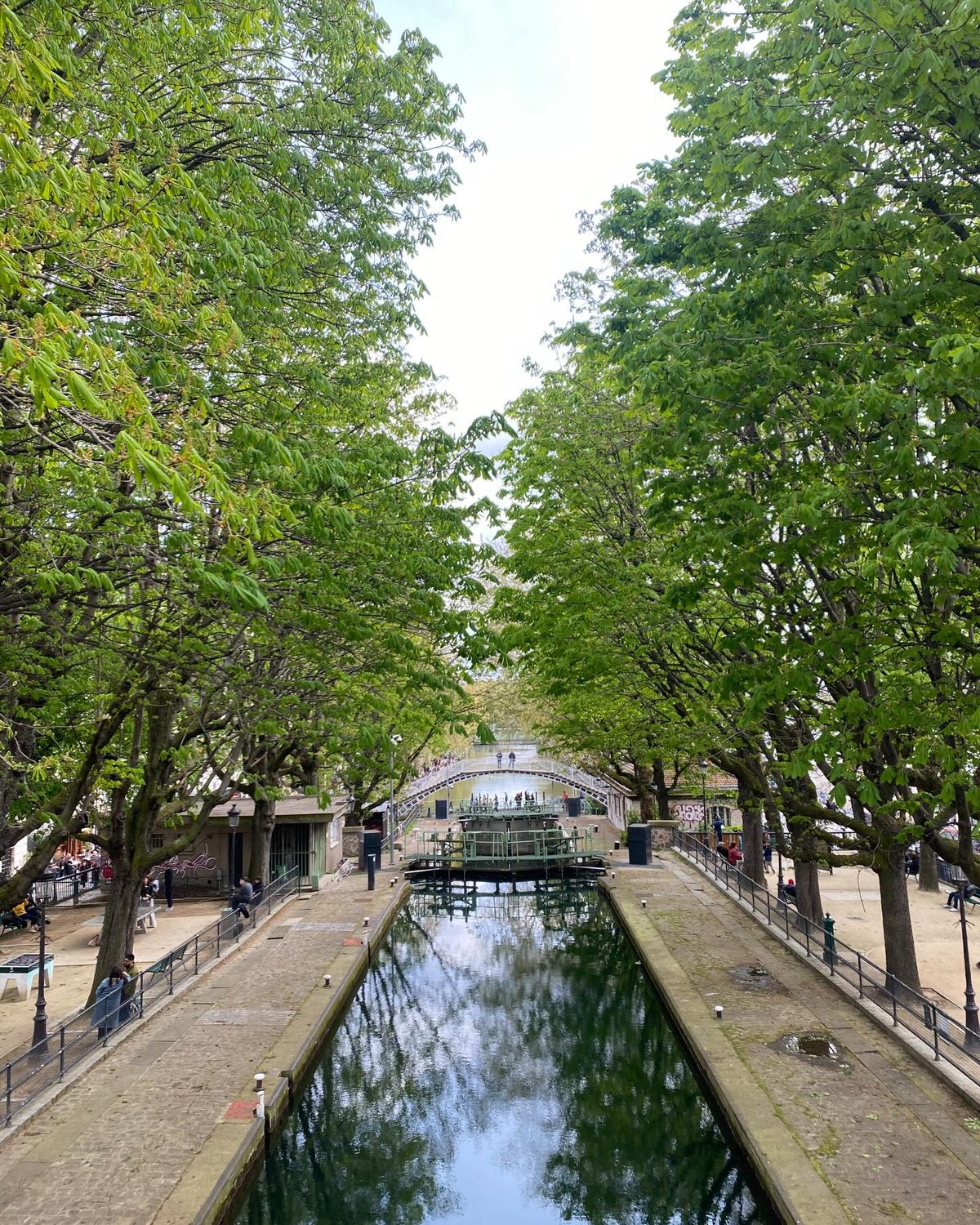 A spring view down the Canal Saint-Martin with chestnut trees in fresh leaf and a footbridge spanning the lock gates in the distance