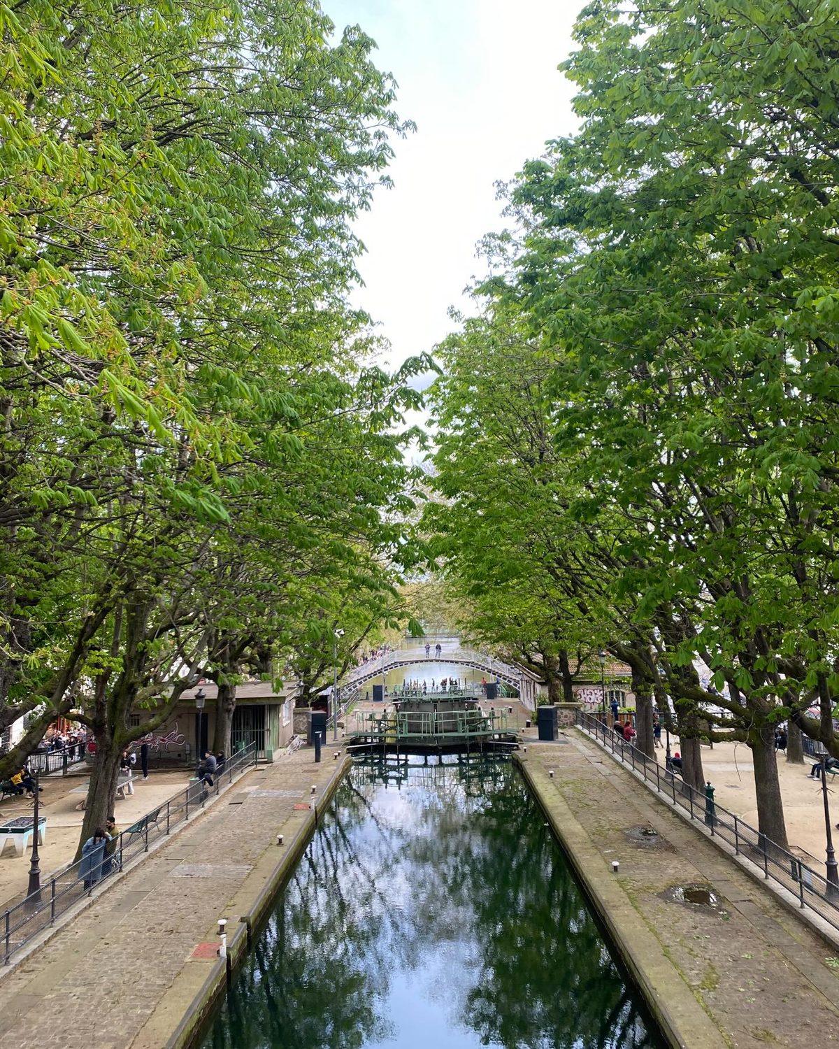 A spring view down the Canal Saint-Martin with chestnut trees in fresh leaf and a footbridge spanning the lock gates in the distance