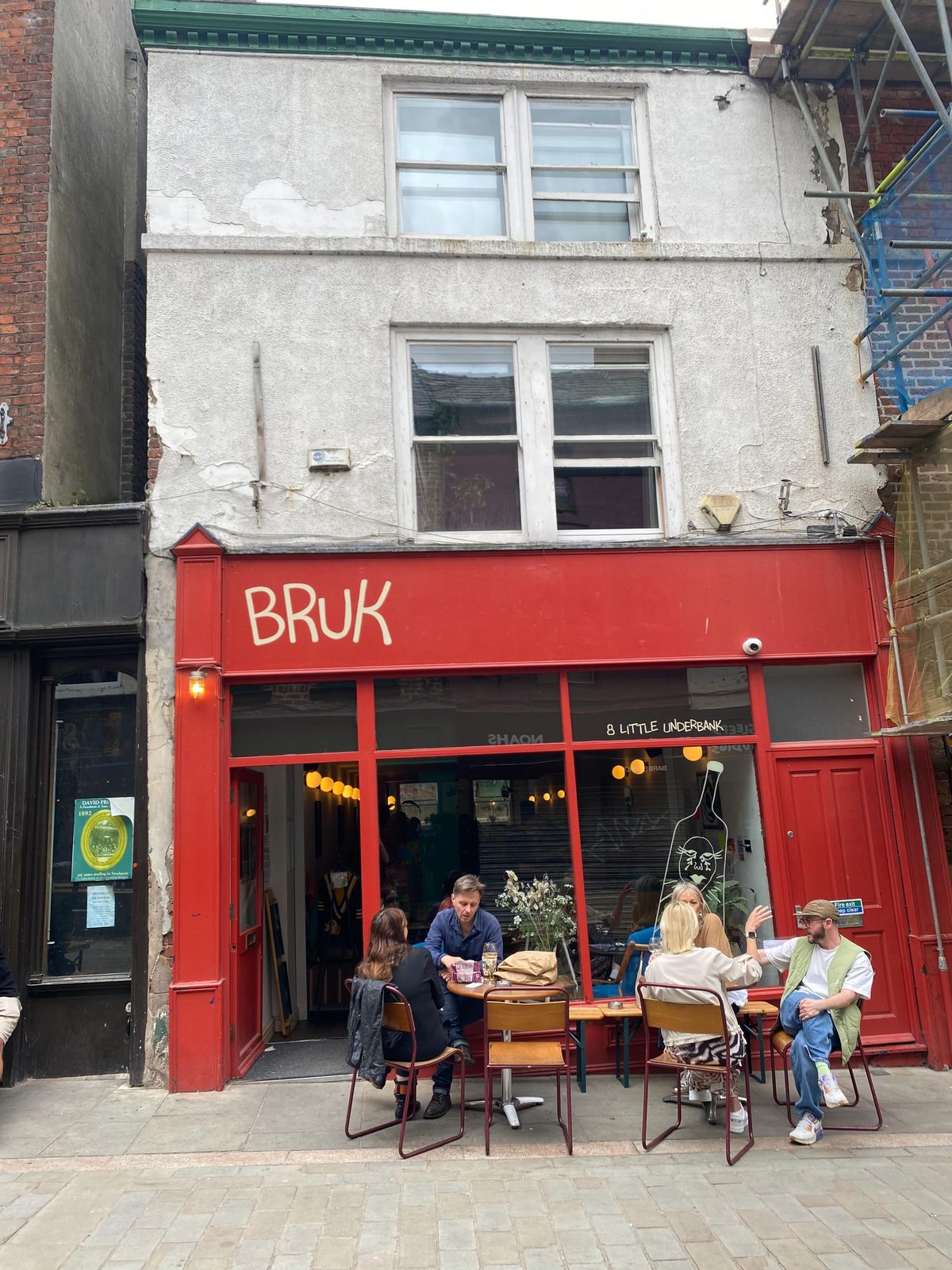 The red shopfront of Bruk on Little Underbank in Stockport, customers seated at small outdoor tables on a sunlit afternoon