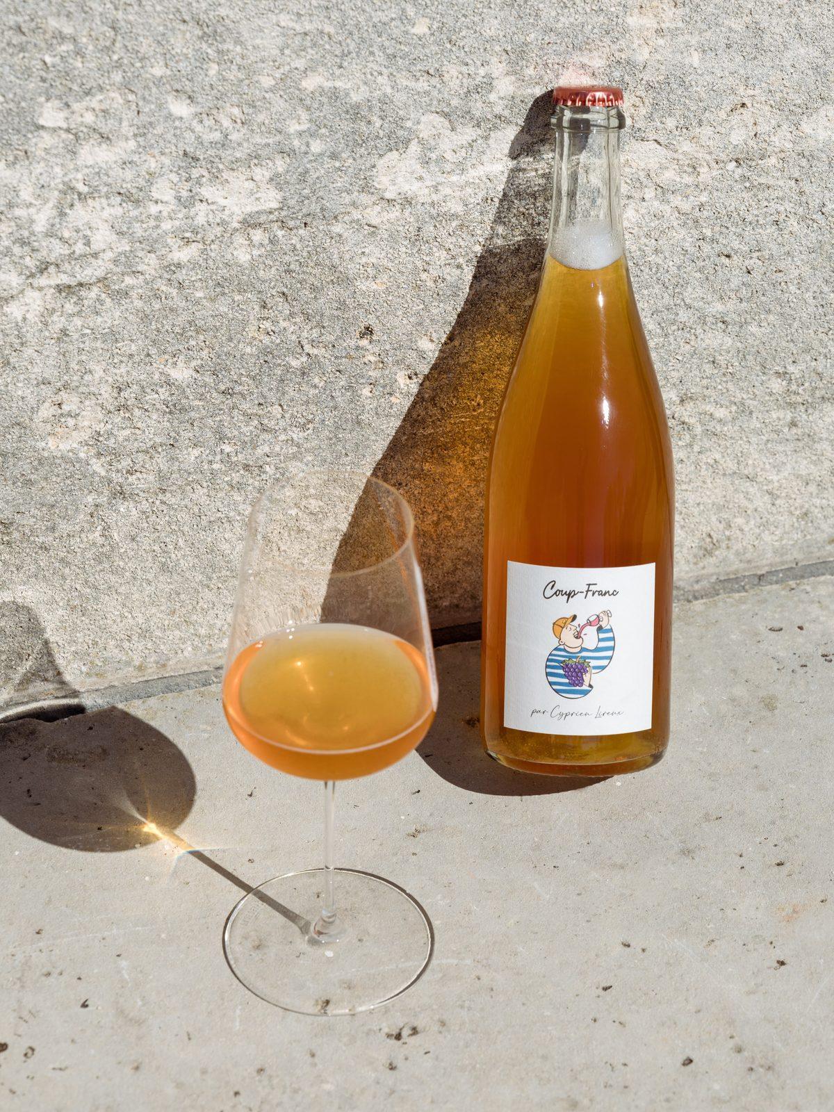 A bottle of Coup-Franc and a poured glass catching the sun on a stone ledge