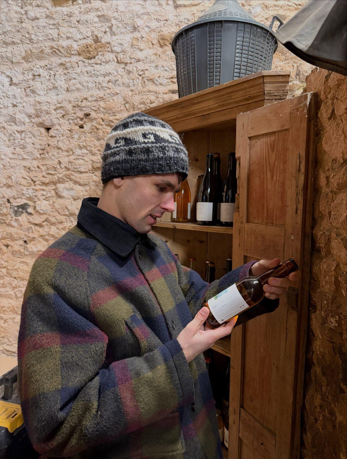 Jack examining a bottle beside a wooden cabinet in the cellar at Domaine Cyprien Lireux