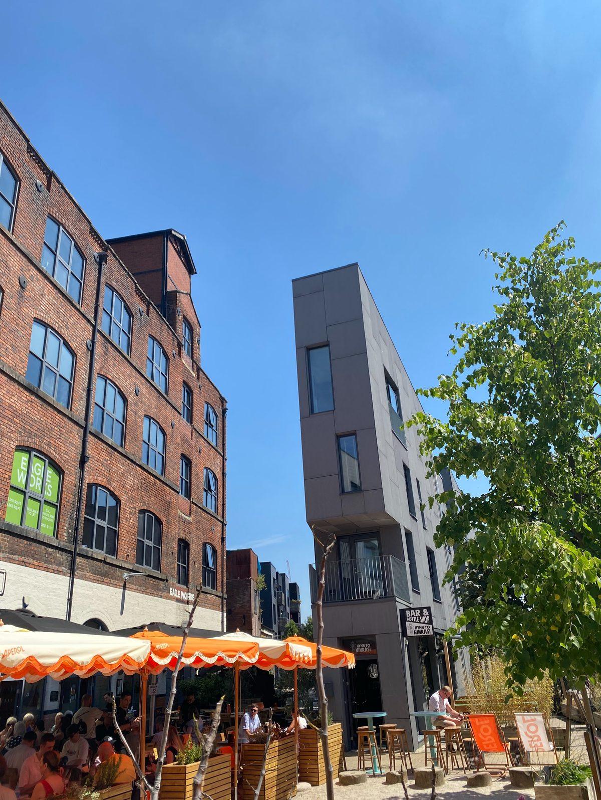 Red-brick mill buildings and orange parasols on a sunny street corner in Kelham Island, Sheffield