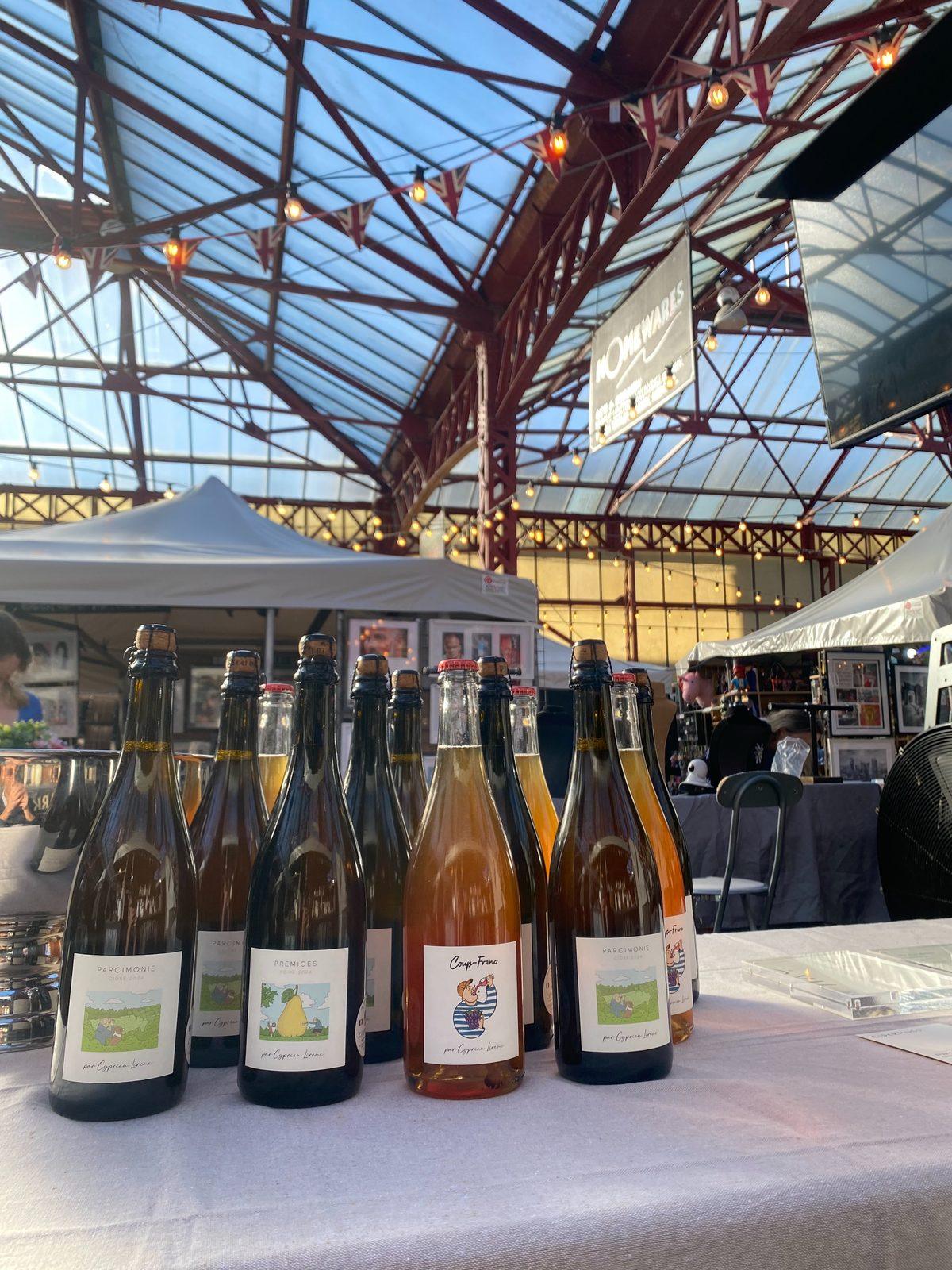 Bottles of the three cuvées lined up on the stall beneath the iron and glass roof of the market hall