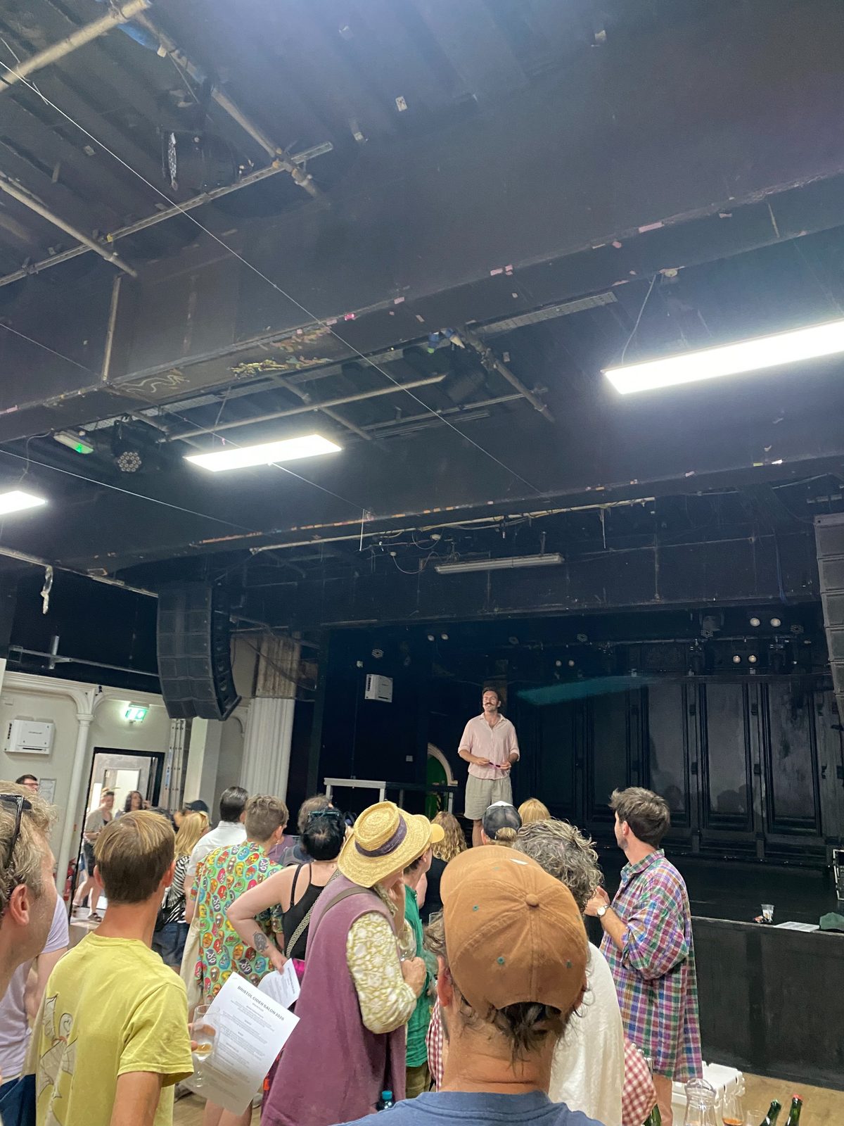 The salon crowd in a Bristol music venue, a speaker addressing the room from the stage