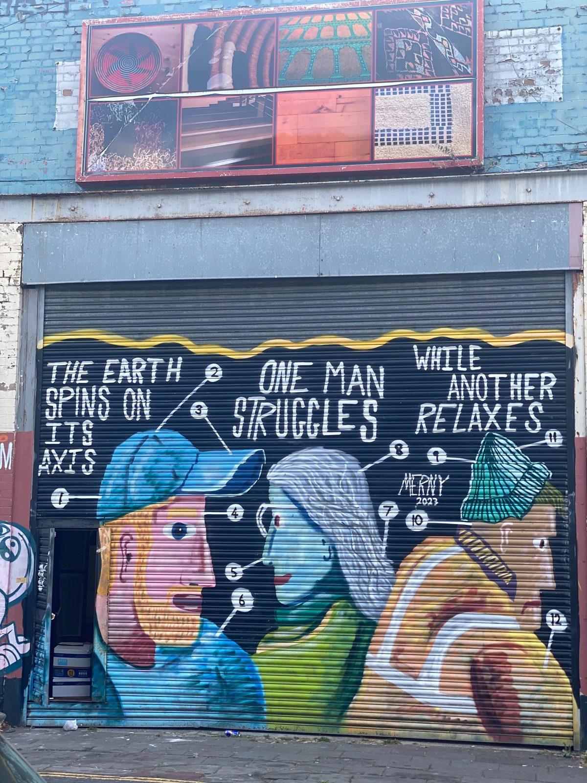A painted shutter mural in Bristol reading 'The earth spins on its axis, one man struggles while another relaxes'
