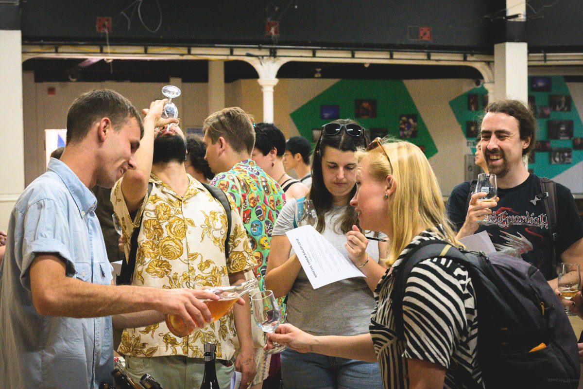 Jack pouring cider for the crowd at Bristol Cider Salon, guests tasting and taking notes in the busy hall